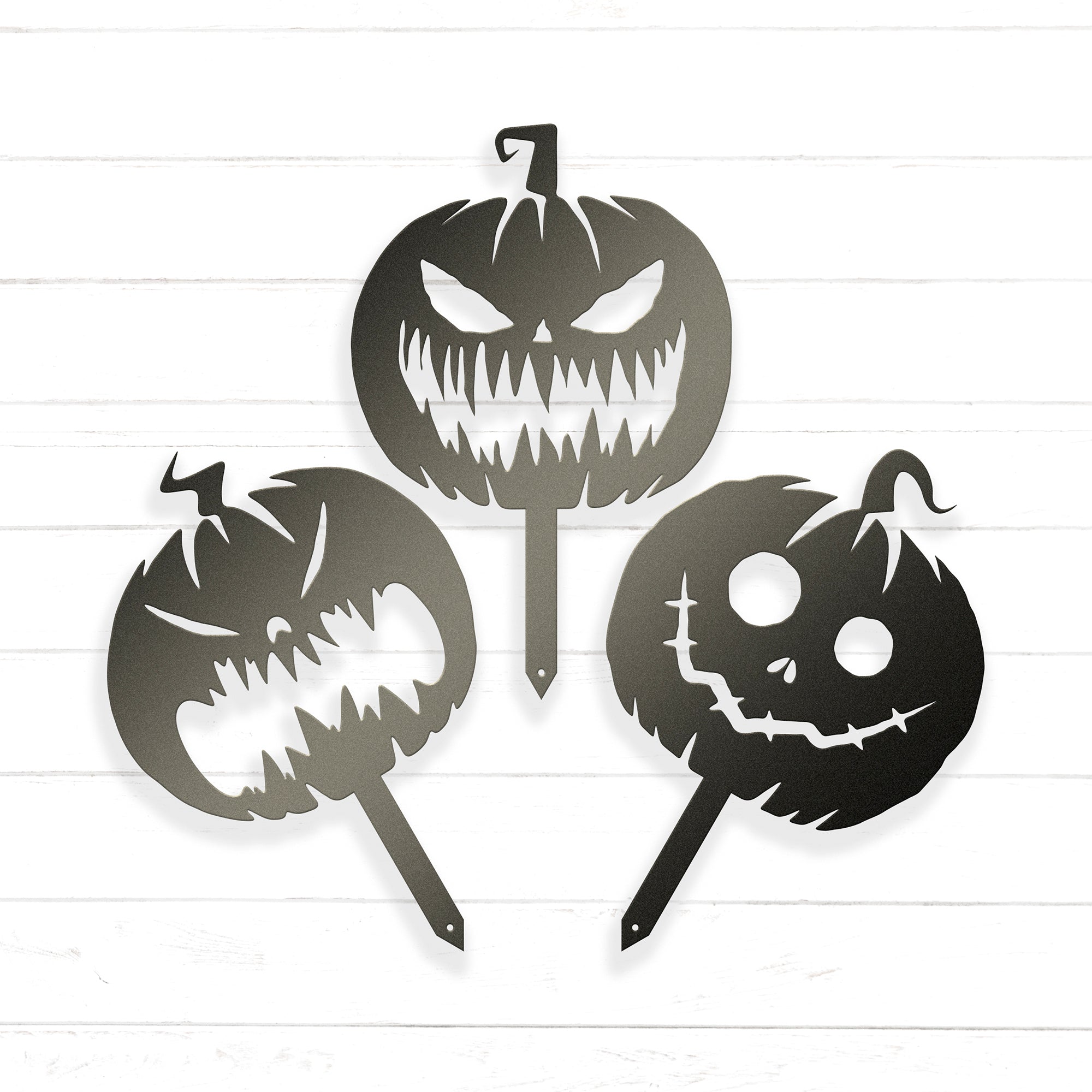 three Halloween-themed cutouts of pumpkins, each with a unique design and expression, arranged in a triangular formation against a white background.