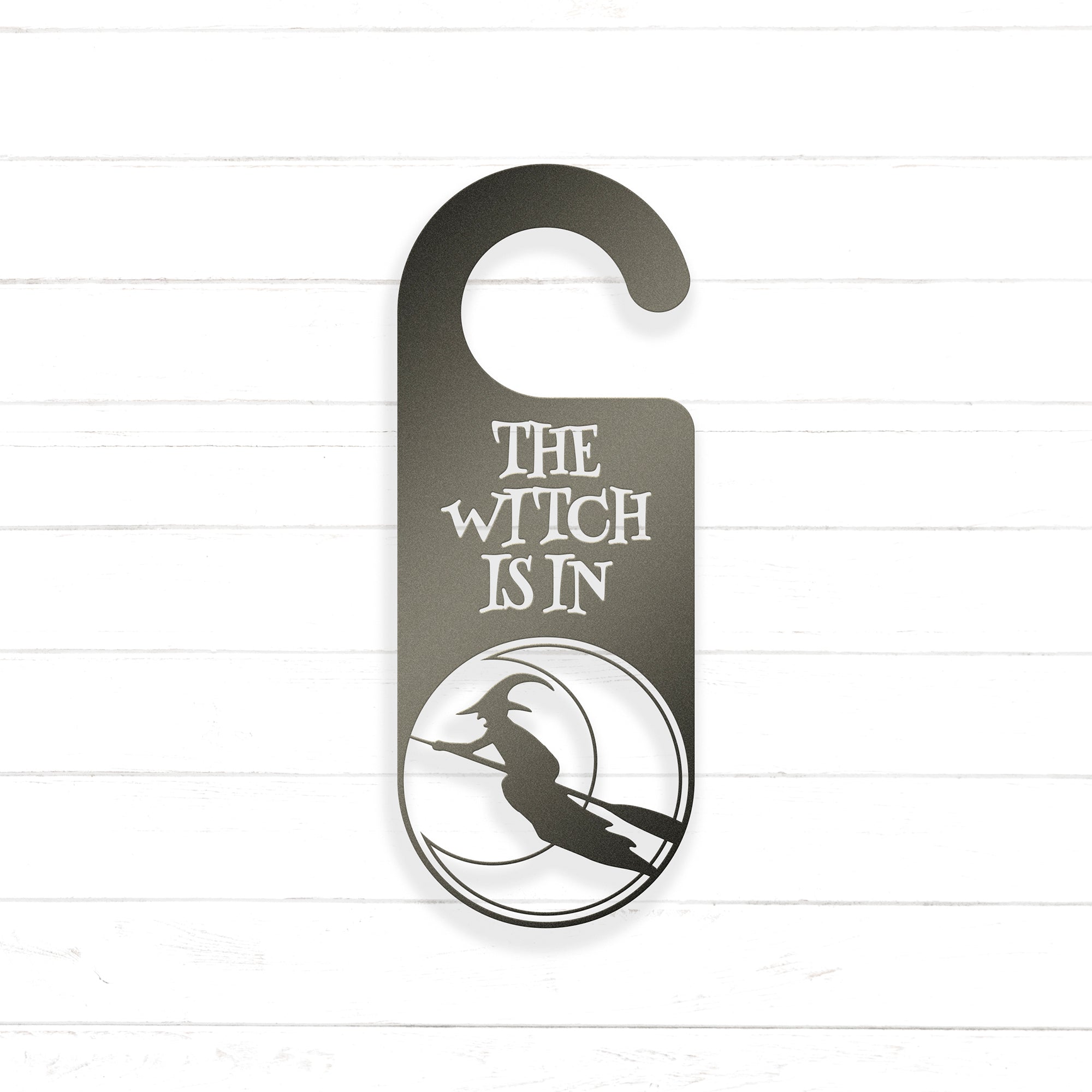 A black and white sign with the text "THE WITCH IS IN" and a silhouette of a witch on a broomstick.
