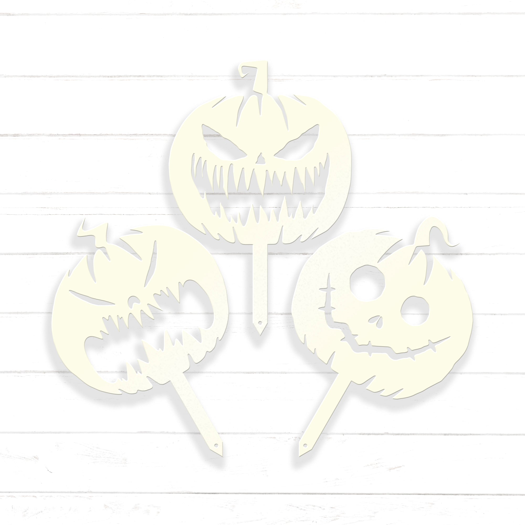 three white paper cutouts of Halloween pumpkins with spooky faces, arranged in a triangular formation against a white background.
