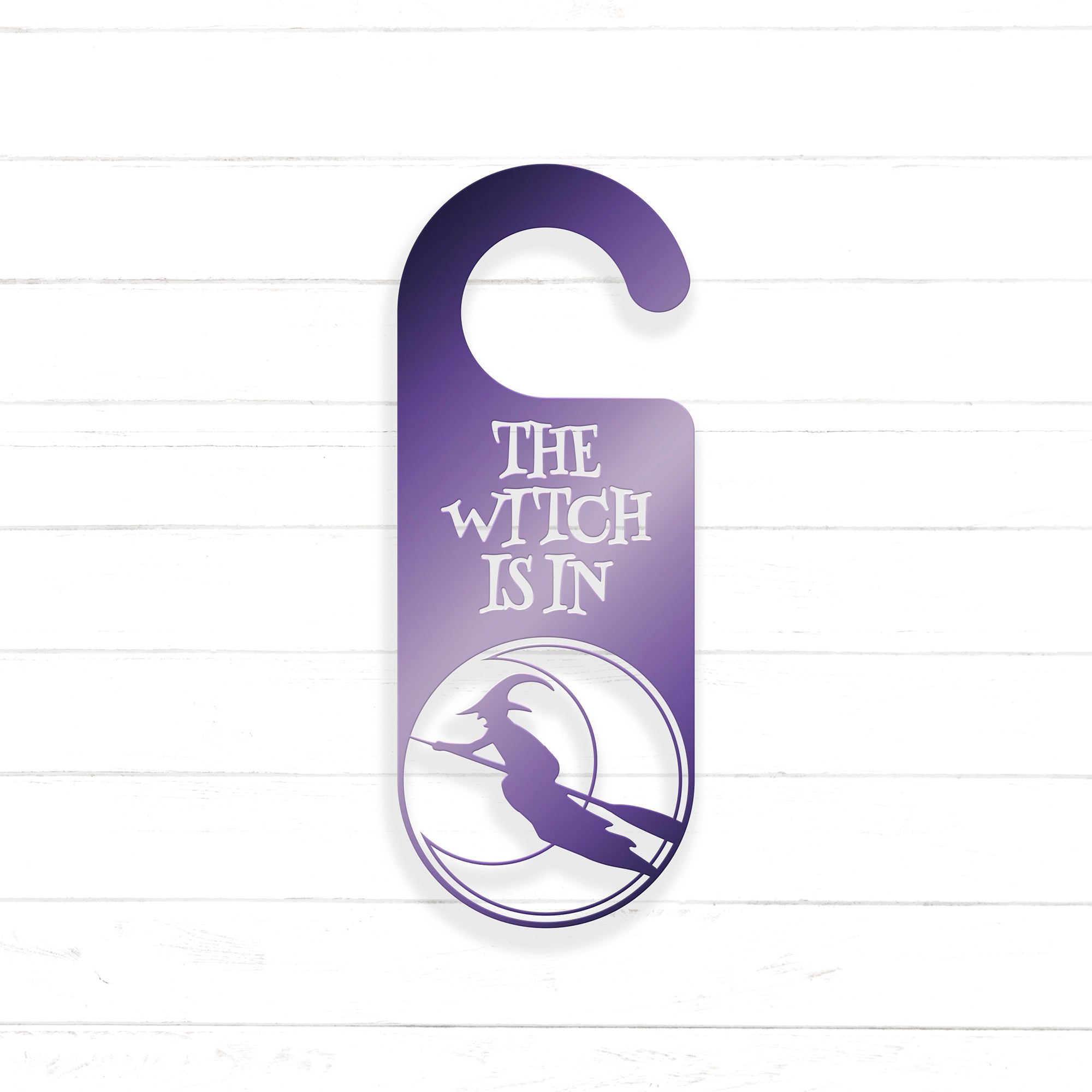 A purple door hanger with the text "THE WITCH IS IN" and a silhouette of a witch on a broomstick.