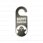 A black and white sign with the text "HAPPY HAUNTING" and a ghost silhouette, hanging on a wooden surface.